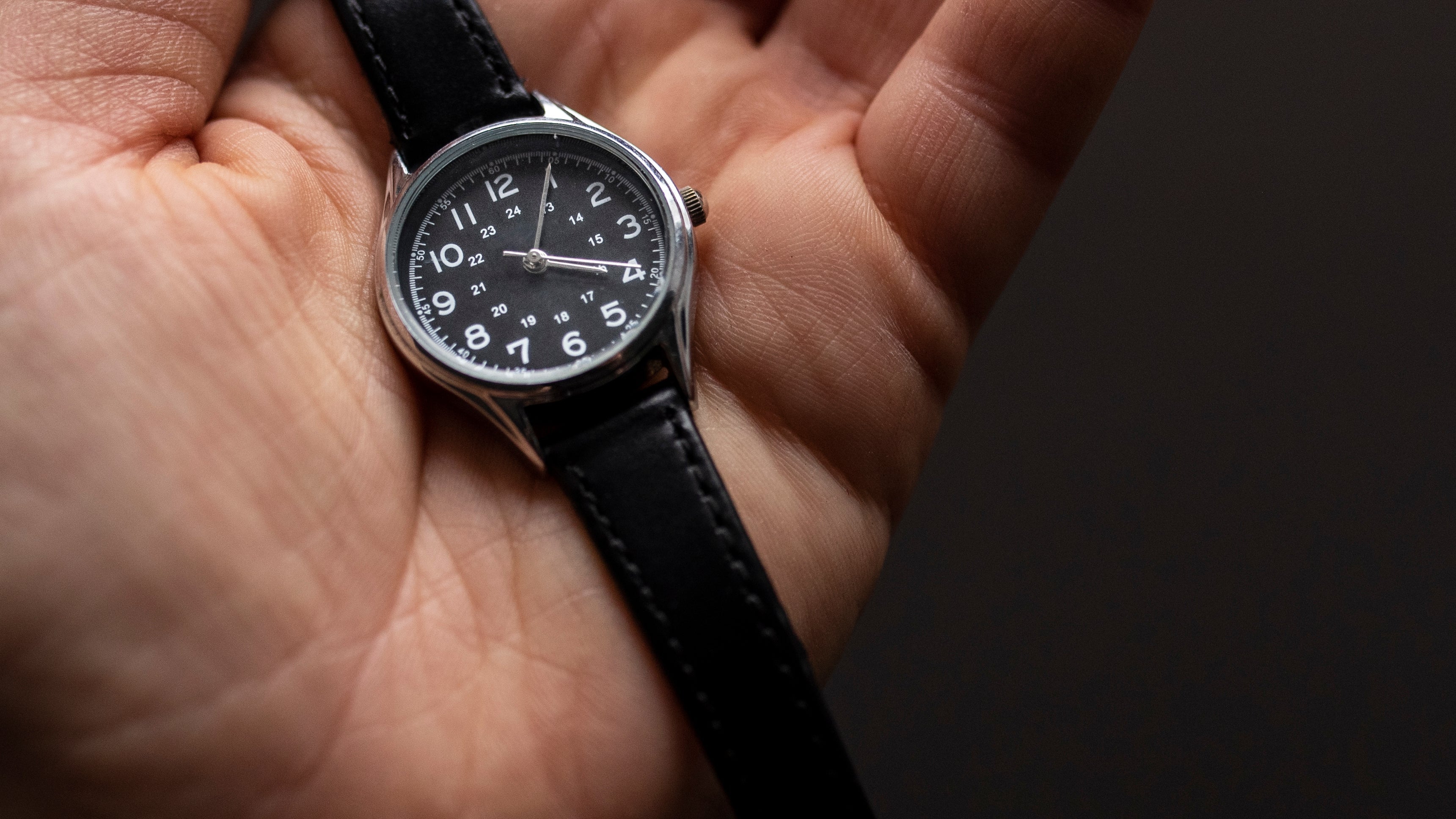 Hand holding a black wristwatch with a dark background